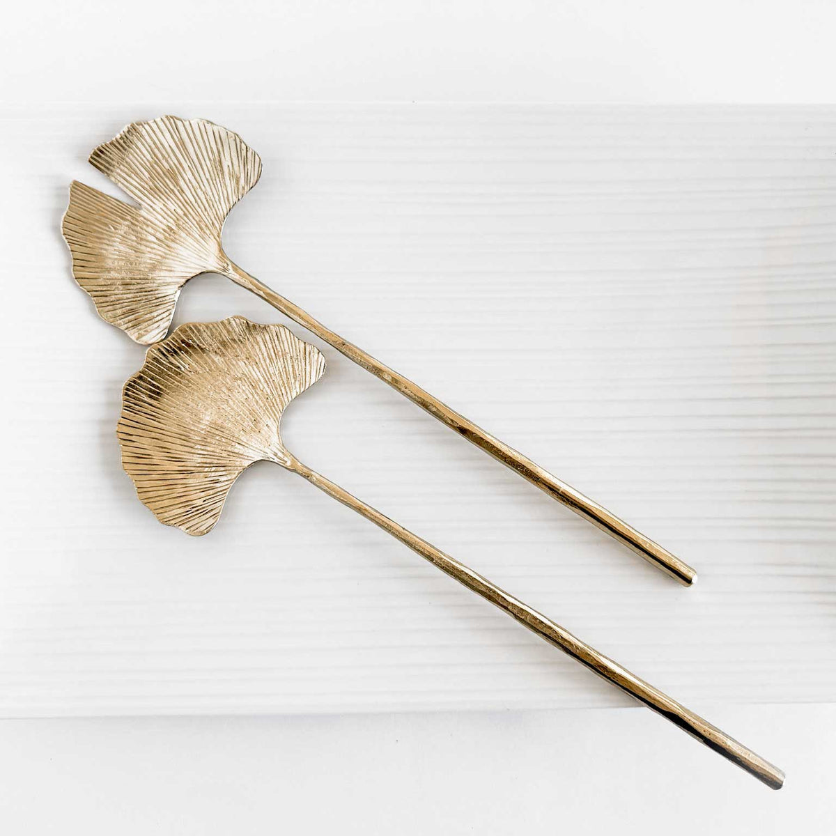 M. By Design - Curated tabletop essentials. Two gold leaf-shaped hairpins on a white background