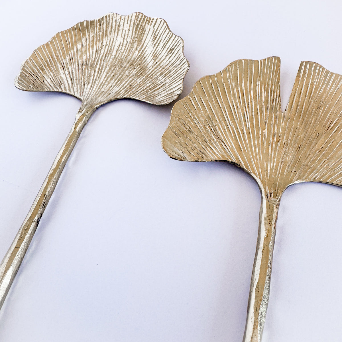 M. By Design - Curated tabletop essentials. Two gold leaf-shaped objects on a light purple background