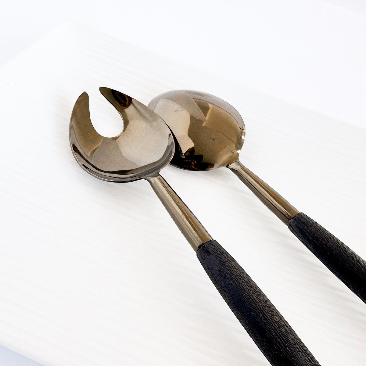 M. By Design - Curated tabletop essentials. Pair of silver tongs with black handles on a white background