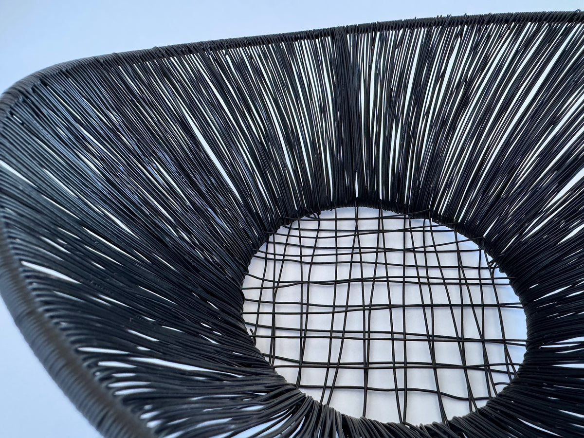 M. By Design - Curated tabletop essentials. Close-up of a woven black basket with a textured pattern on a light blue background